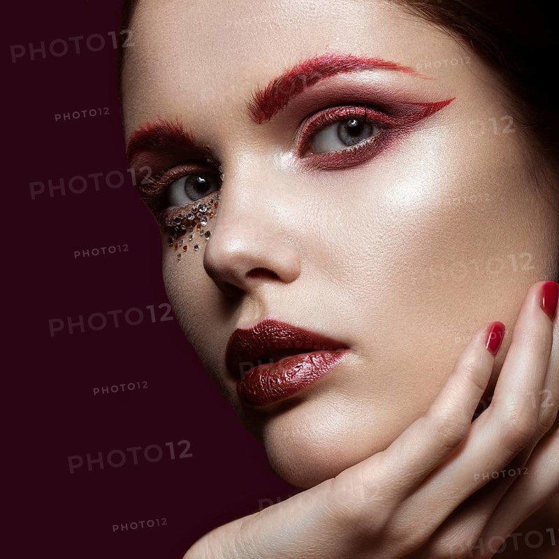 Beautiful girl with a bright red fashion makeup and crystals on the face. Close-up portrait. Beauty face. Picture taken in the studio