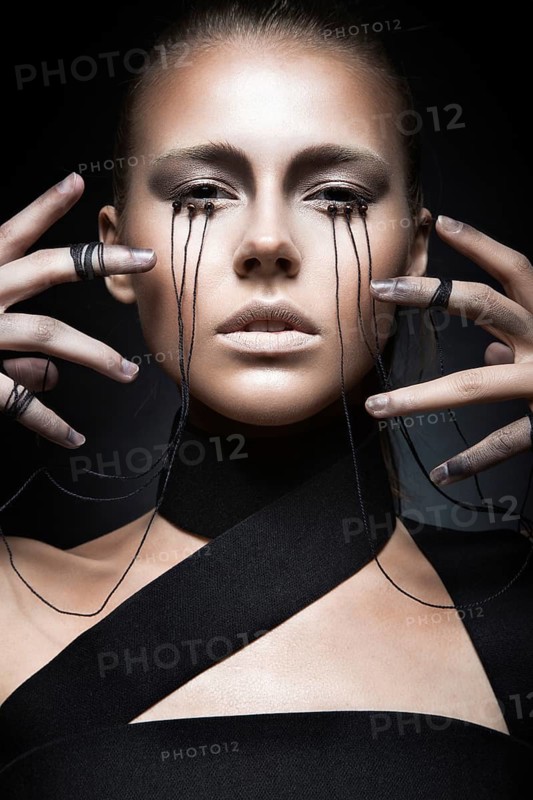 Beautiful girl with creative make-up in Gothic style and the threads of eyes. Art beauty face. Picture taken in the studio on a black background