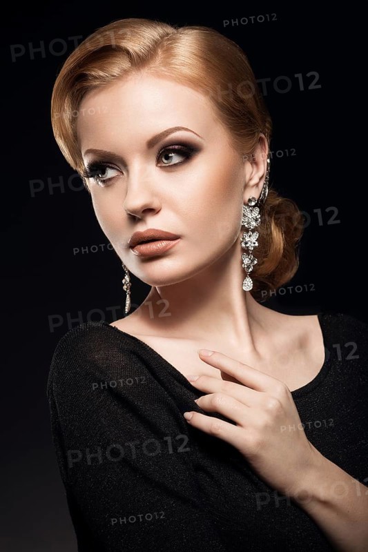 Beautiful red-haired girl in a black dress with a smooth evening haircut in the form of waves and bright makeup. Beauty face. Picture taken in the studio on a black background