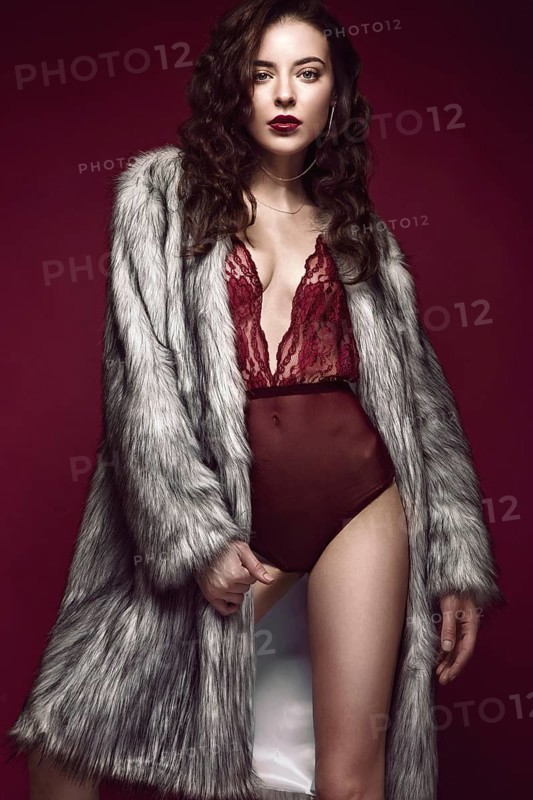 Beautiful sexy long-haired brunette woman in red lingerie and fur coat posing in the studio. The beauty of the face and body. Photos shot in a studio