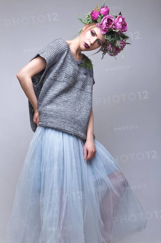 Beautiful girl with flowers on her head in fashion clothes posing against the background in the studio. Beauty Style