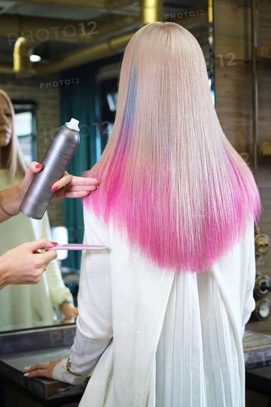 Beautiful blond girl with colored pink hair in a hairdressing salon. The client looks at herself in the mirror