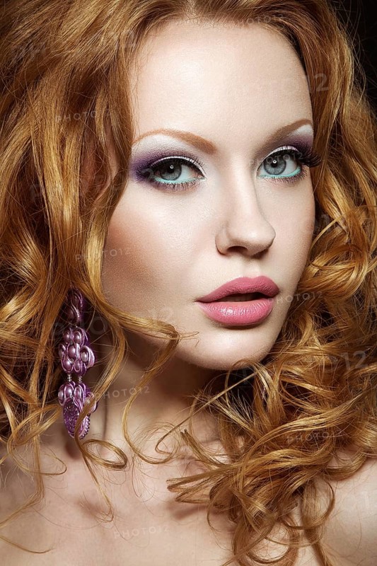 Beautiful red-haired girl with bright makeup and curls. Picture taken in the studio on a black background