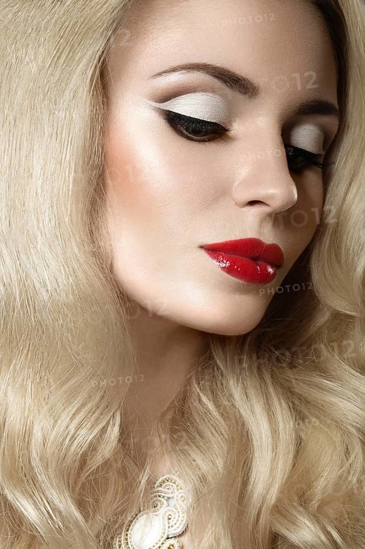 Beautiful blonde woman with evening make-up and red lips. Picture taken in the studio on a black background