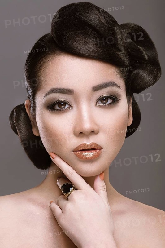 Beautiful girl with oriental type evening hair and makeup. Portrait shot in the studio on a gray background