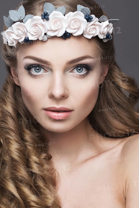 Portrait of a beautiful girl with a wreath of pink flowers on her head. Photo shot in the Studio on a grey background