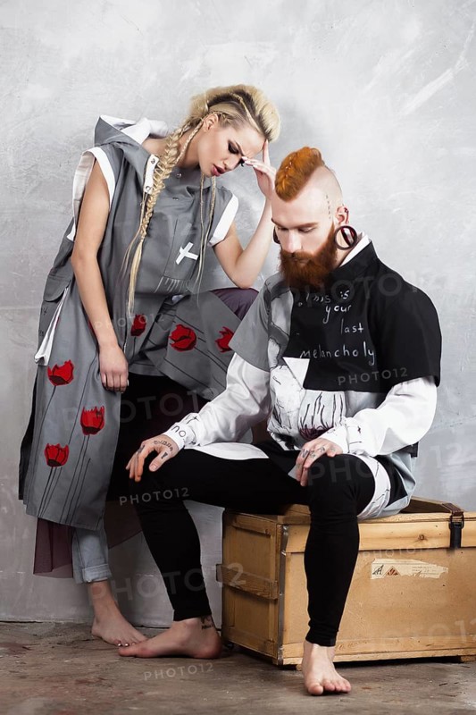 Creative unusual blond girl and red-haired man in designer clothes and braids on their heads posing in the studio