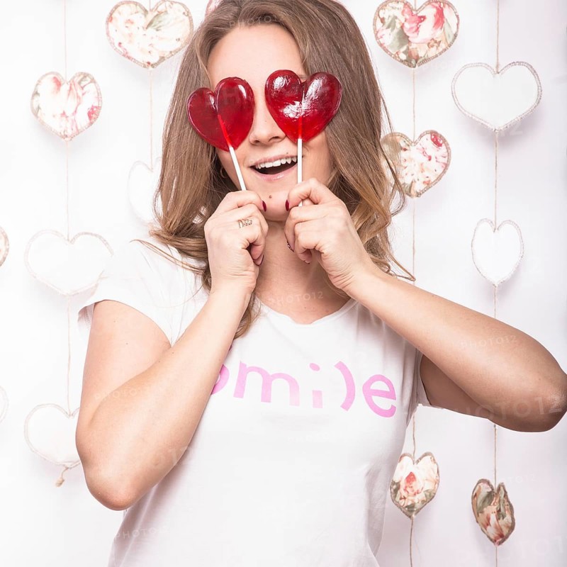 Valentines Day. Funny beautiful Woman holding candy in the form of heart. Beauty face. Picture taken in the studio with decorations