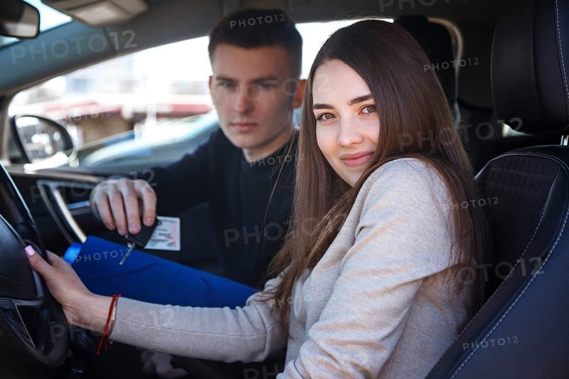Happy girl in a new car receives a drivers license and keys from a young man