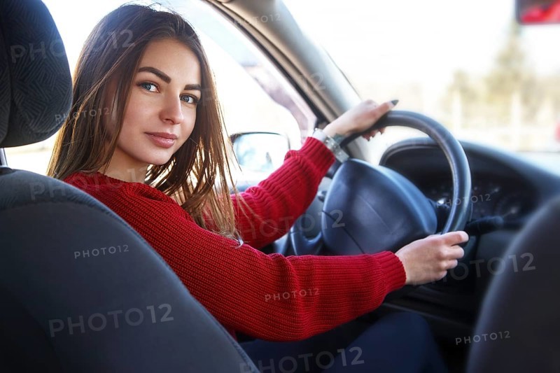 Young beautiful happy woman in red sitting at the wheel new training car