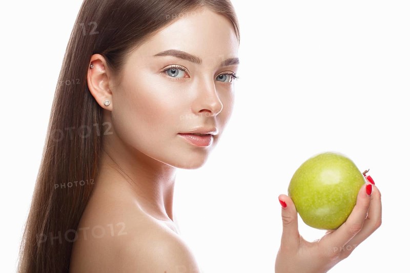 Beautiful young girl with a light natural make-up and perfect skin with apple in her hand. Beauty face. Picture taken in the studio on a white background