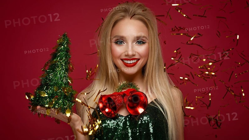 Beautiful blonde girl in a New Year's image with Christmas bells around her neck and green tree. Beauty face with festive makeup. Photo taken in the studio