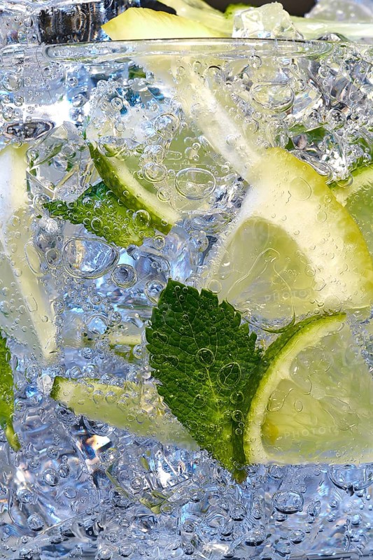 Glass of Mojito summer alcoholic cocktail with ice cubes mint and lime on white background with raw lime and mint leaf