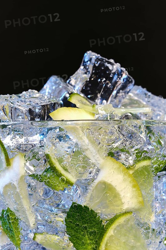 Glass of Mojito summer alcoholic cocktail with ice cubes mint and lime on black background with raw lime and mint leaf