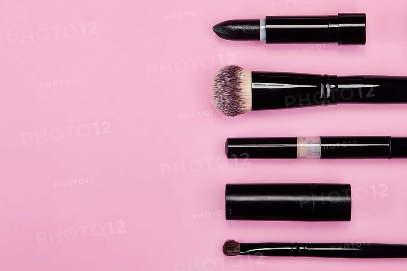 Set of brushes and cosmetic products on a pink background