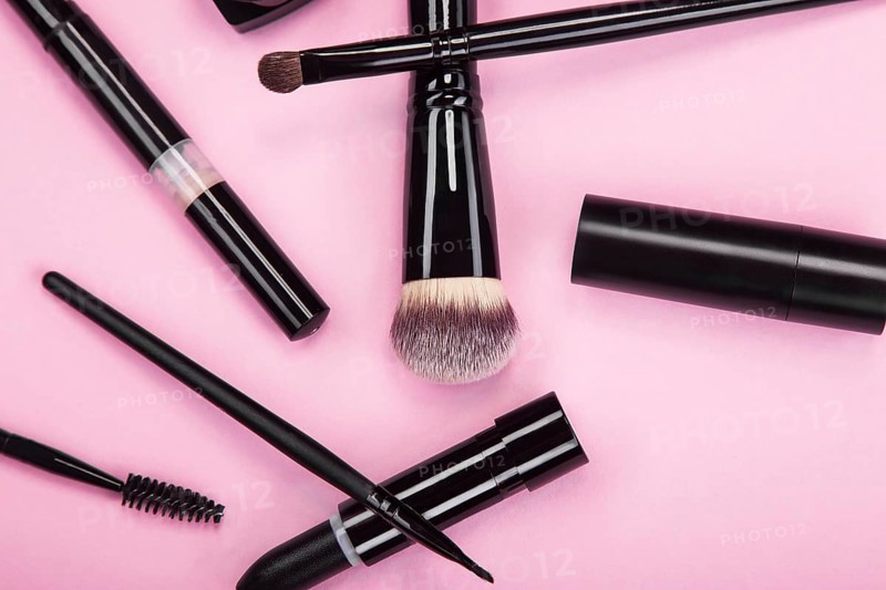 Set of brushes and cosmetic products on a pink background
