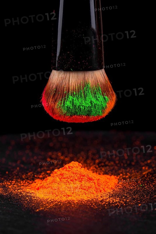 Cheek brush with neon cosmetic powder colorful pile and isolated on black background