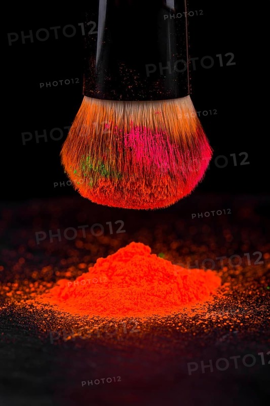 Cheek brush with neon cosmetic powder colorful pile and isolated on black background