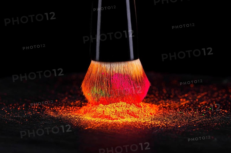 Cheek brush with neon cosmetic powder colorful pile and isolated on black background