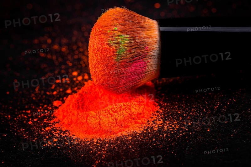 Cheek brush with neon cosmetic powder colorful pile and isolated on black background