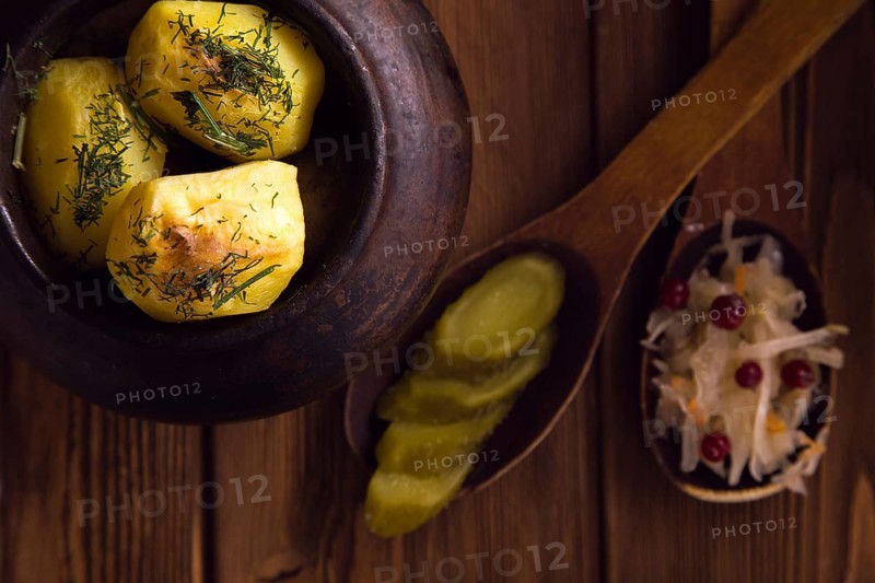 Baked potato in old pot on wooden background with pickled cabbage and cucumber