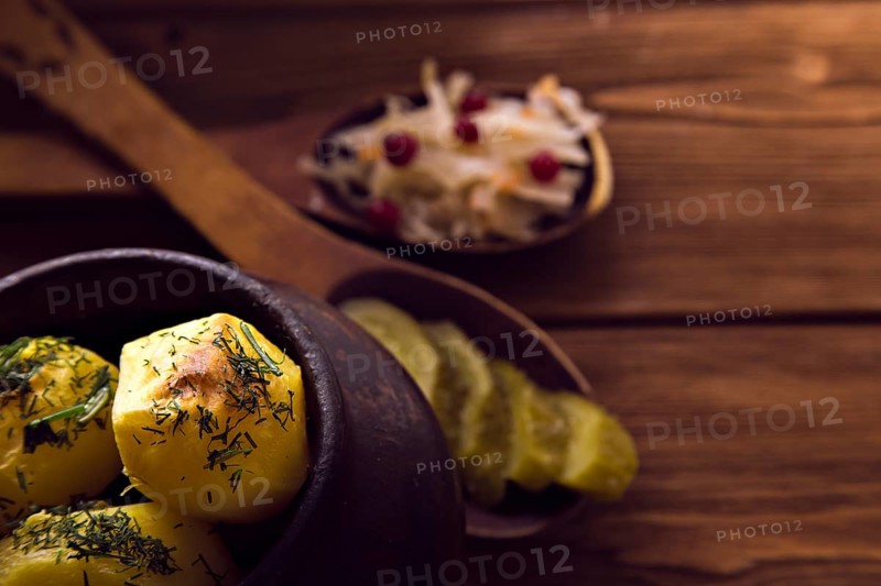 Baked potato in old pot on wooden background with pickled cabbage and cucumber