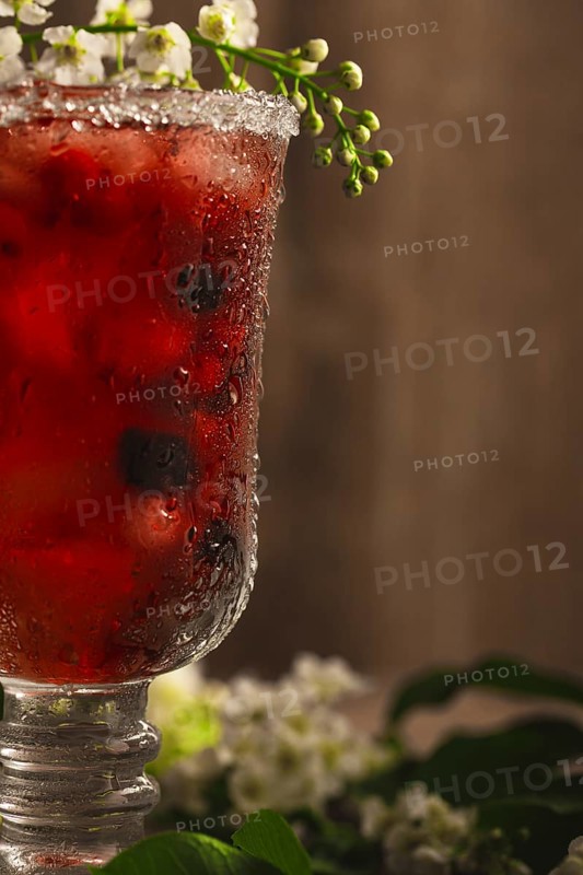 Berry soft drink with ice on a wooden background with flowers