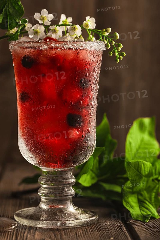 Berry soft drink with ice on a wooden background with flowers