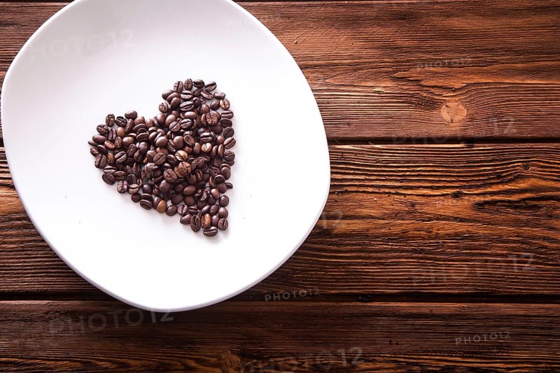 Grains of roasted coffee in the shape of heart on a white plate