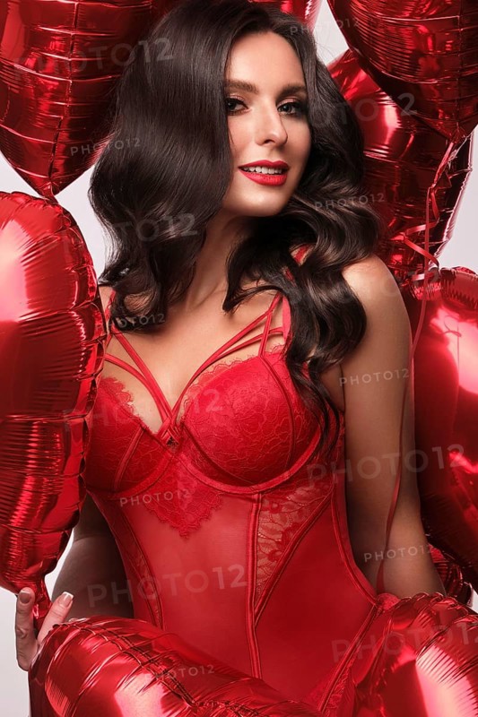 Sexy woman in red lace lingerie and balloons with hearts posing in the studio on Valentine's Day