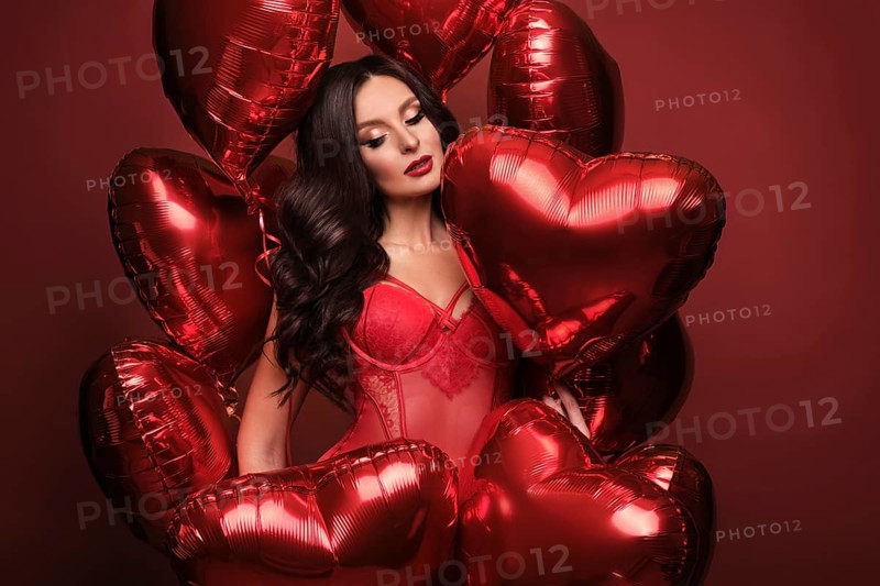 Sexy woman in red lace lingerie and balloons with hearts posing in the studio on Valentine's Day