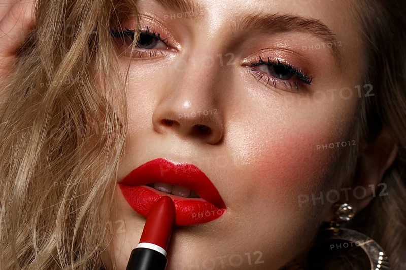 Beautiful girl with red lips and classic makeup and curls with lipstick in hand. Beauty face. Photo taken in the studio