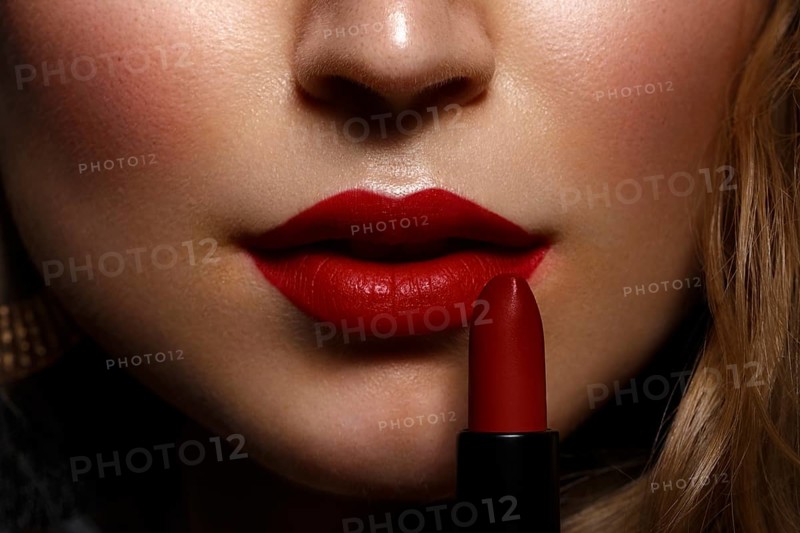Beautiful girl with red lips and classic makeup and curls with lipstick in hand. Beauty face. Photo taken in the studio