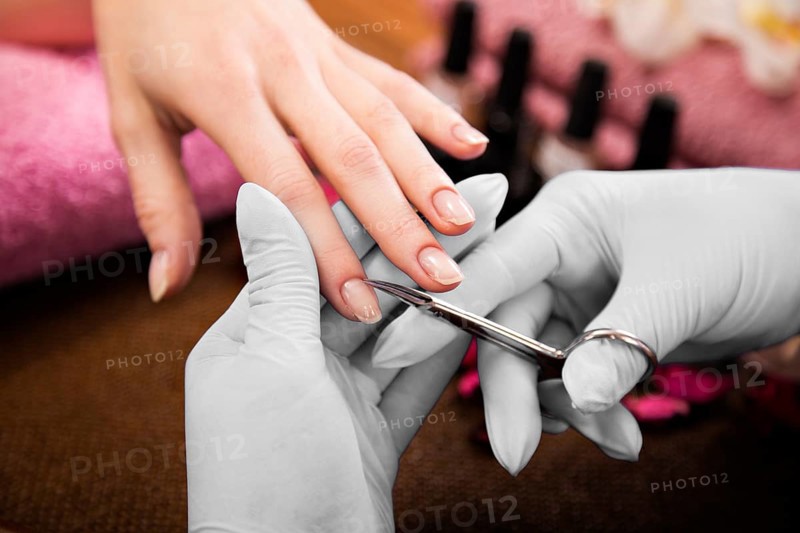 Closeup finger nail care by manicure specialist in beauty salon. Manicurist clear cuticle professional scissors for manicure and pedicure
