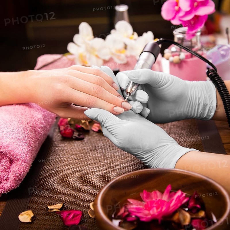 Closeup finger nail care by manicure specialist in beauty salon. Manicurist clear cuticle professional electric tool for manicure and pedicure
