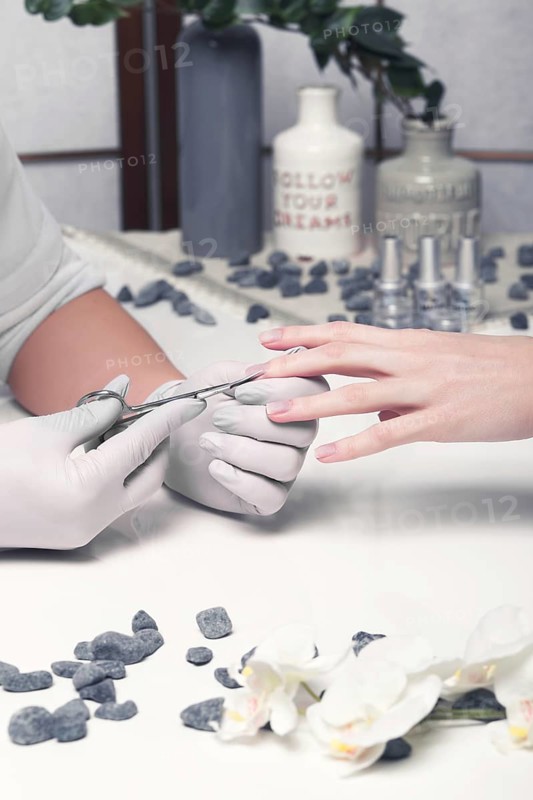 Closeup finger nail care by manicure specialist in beauty salon. Manicurist clear cuticle professional scissors for manicure and pedicure