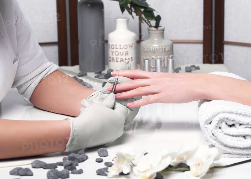 Closeup finger nail care by manicure specialist in beauty salon. Manicurist clear cuticle professional scissors for manicure and pedicure