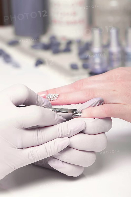 Closeup finger nail care by manicure specialist in beauty salon. Manicurist paints nails with nail polish