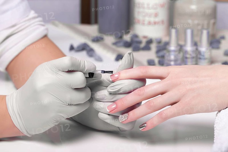 Closeup finger nail care by manicure specialist in beauty salon. Manicurist paints nails with nail polish