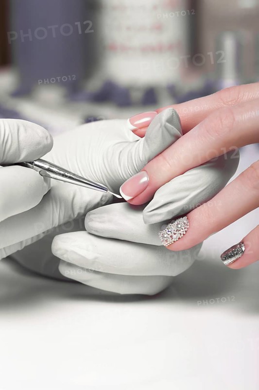 Closeup finger nail care by manicure specialist in beauty salon. Manicurist paints nails with nail polish