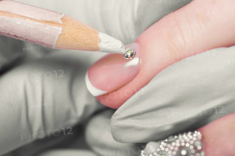 Closeup finger nail care by manicure specialist in beauty salon. Manicurist Glues rhinestones on nails