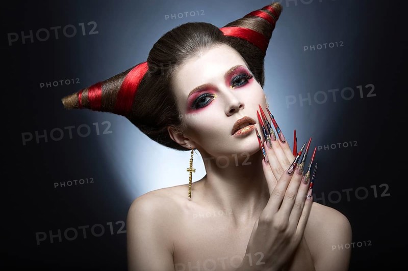 The girl in an image of the demon-tempter with long nails and haircut in the form of horns. Picture taken in the studio on a gray background