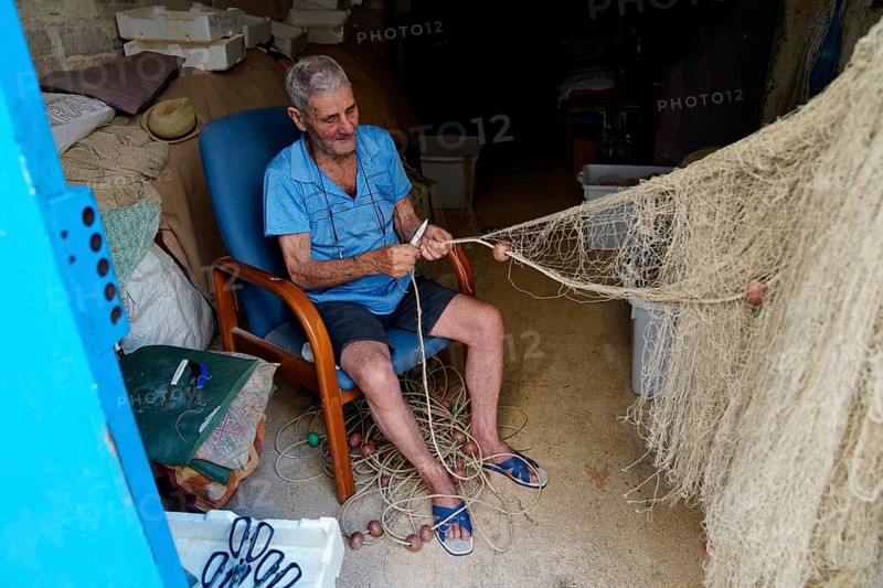 Old fisherman repairing nets