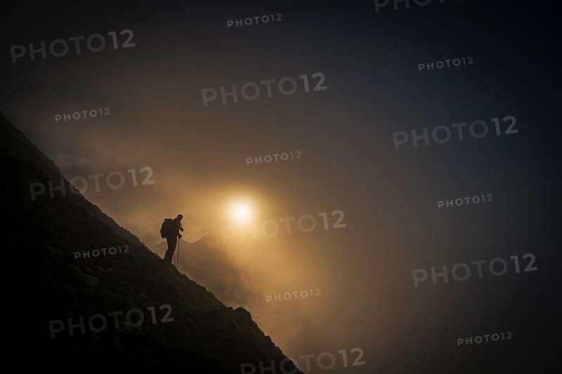 Mountaineer on mountain slope with fog against the light