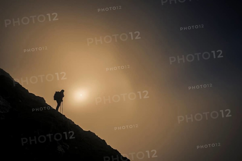 Mountaineer on mountain slope with fog against the light