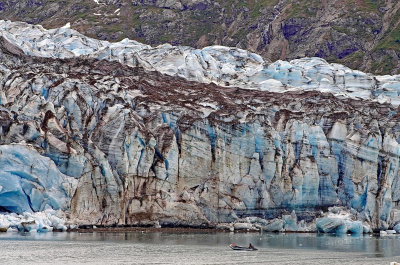 Small boat with two people in front of the huge front of a glacier