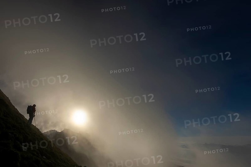 Mountaineer on mountain slope with fog against the light