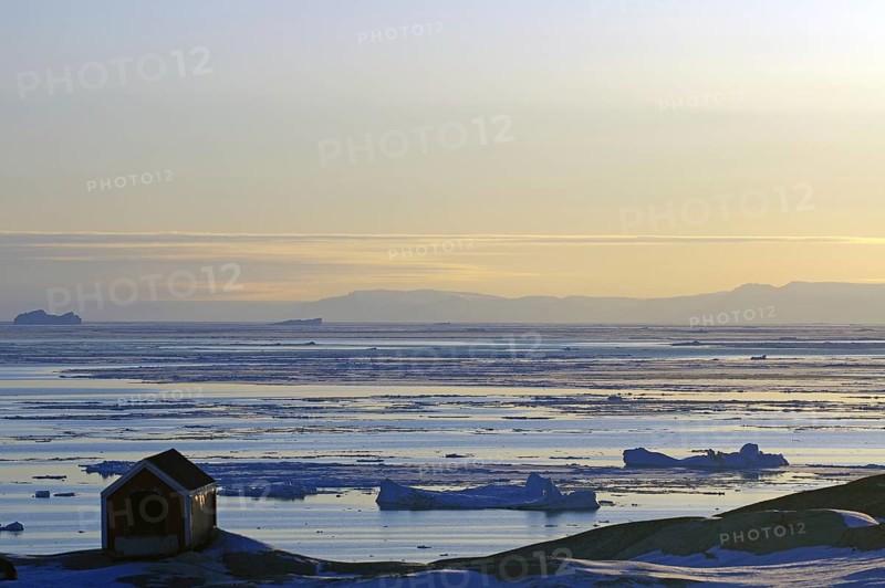Doghouse standing on rocks in front of a bay littered with icebergs