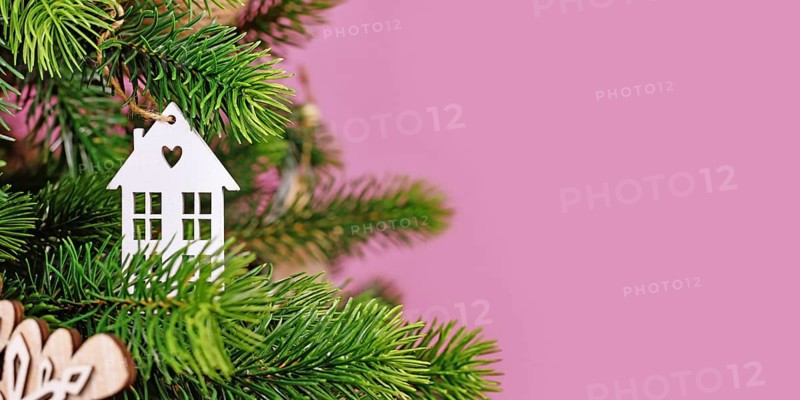Banner with Christmas tree decorated with white house shaped tree ornament baubles on pink background with empty copy space