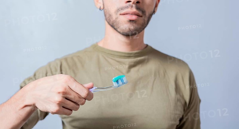 Guy with unrecognizable face holds brush with toothpaste on isolated background